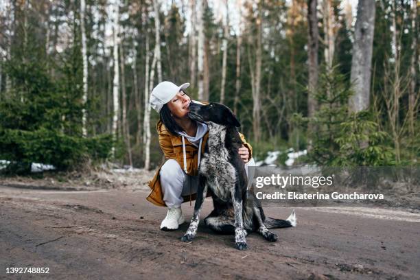 portrait of a woman in a yellow jacket walking through the woods with a dog in cool weather - frauen hund park stock-fotos und bilder