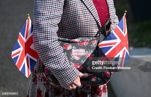 Woman holds a Cath Kidston handbag and Union Jack flags as she waits for Princess Anne, Princess Royal during her visit to view the D-Day landing...