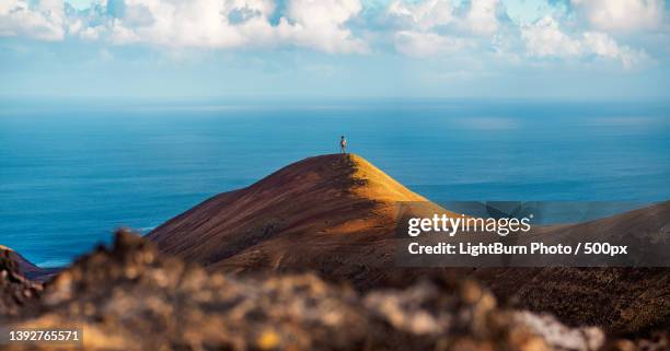 long lens view of person standing on mountain top against scenic view and sky,lanzarote,las palmas,spain - paysage volcanique photos et images de collection