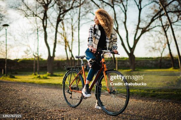 woman prepares for bicycle ride in public park at sunset - bicycle safety light stockfoto's en -beelden