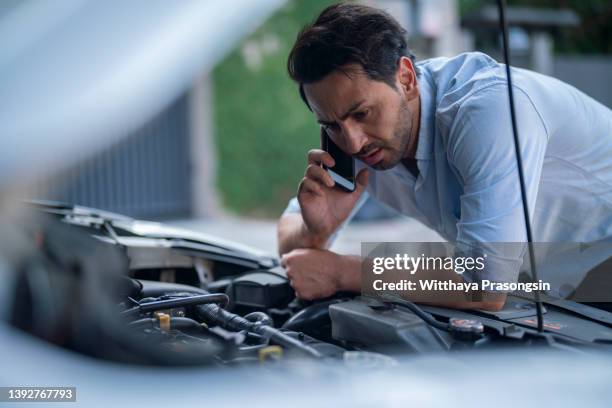 young man calling for road assistance, standing next to a broken down car - car broken down stock-fotos und bilder