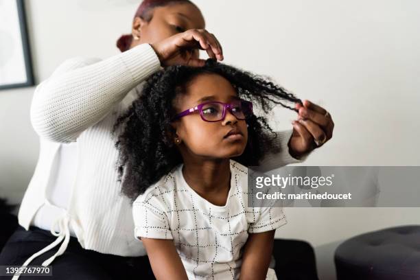 mother undoing braids of young daughter in living room. - natural black hair stock pictures, royalty-free photos & images