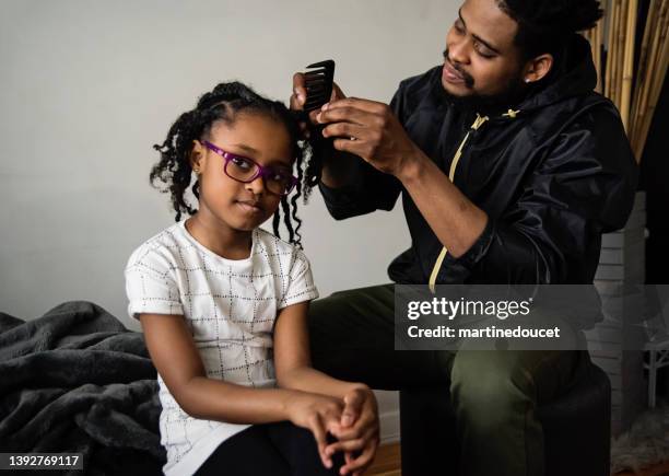 father undoing braids of young daughter in living room. - afro caribbean ethnicity stock pictures, royalty-free photos & images