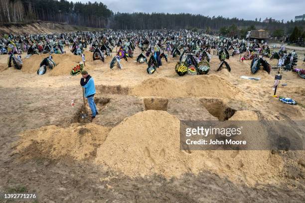 Grave digger pauses while preparing the ground for a funeral at a cemetery on April 21, 2022 in Irpin, Ukraine. The first several rows contain people...