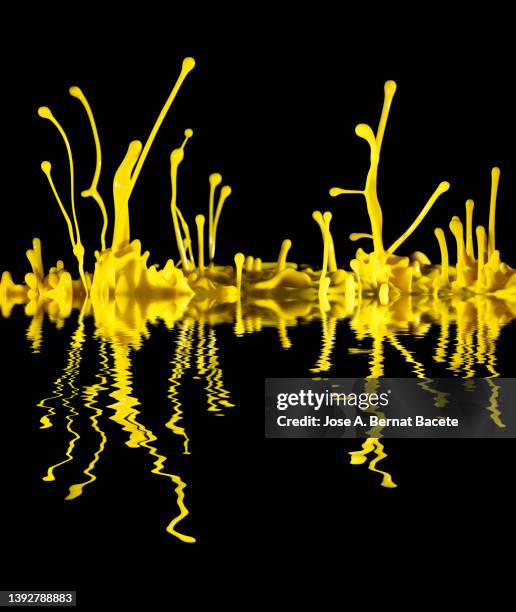 drops and splashes of yellow paint in motion on a black background reflected on a water surface. - changing form photos et images de collection