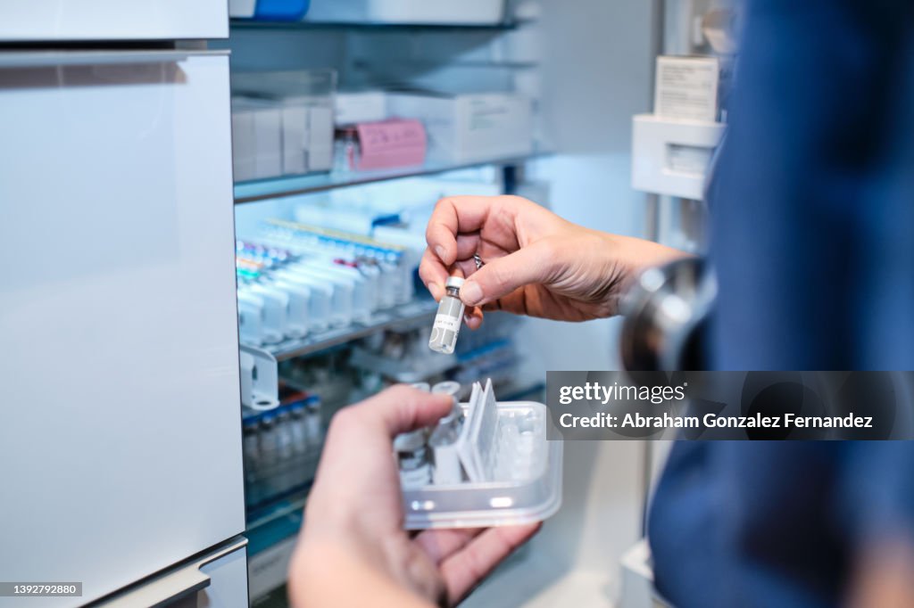 Unrecognizable nurse takes vial of liquid medication from refrigerator shelf