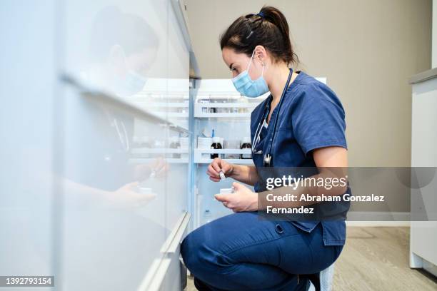 a nurse wearing a mask taking a vial of liquid medication from the refrigerator shelf - prevenção de doenças - fotografias e filmes do acervo