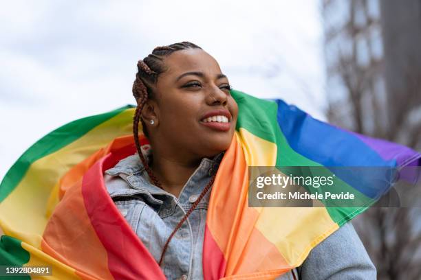 donna nera sicura di sé all'aperto con in mano una bandiera arcobaleno - diritti degli omosessuali foto e immagini stock