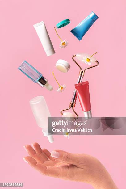 woman hand holds  flying skin care products on pastel pink color background. - drug gefabriceerd object stockfoto's en -beelden