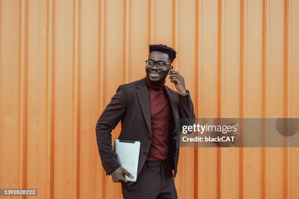 porträt eines jungen lächelnden afroamerikanischen geschäftsmannes vor der orangefarbenen wand - smart fashion stock-fotos und bilder