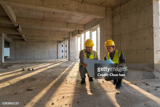 male and female construction engineers with drawings comparing data - construction industry stock pictures, royalty-free photos & images