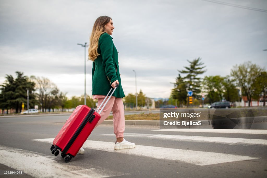 Young woman walking and pulling wheeled luggage on her way to the airport