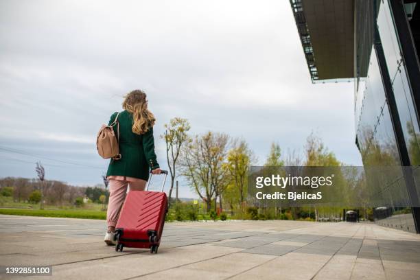 geschäftsfrau mit koffer auf dem weg zum flughafen - young woman trolley stock-fotos und bilder