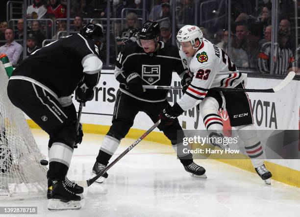 Philipp Kurashev of the Chicago Blackhawks plays the puck as he is checked by Carl Grundstrom and Alexander Edler of the Los Angeles Kings during the...