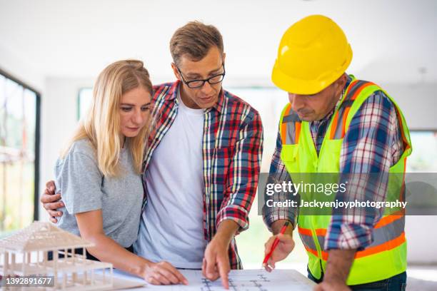 engineer talking to couple in unfinished house about their blueprint - new home owners stock-fotos und bilder