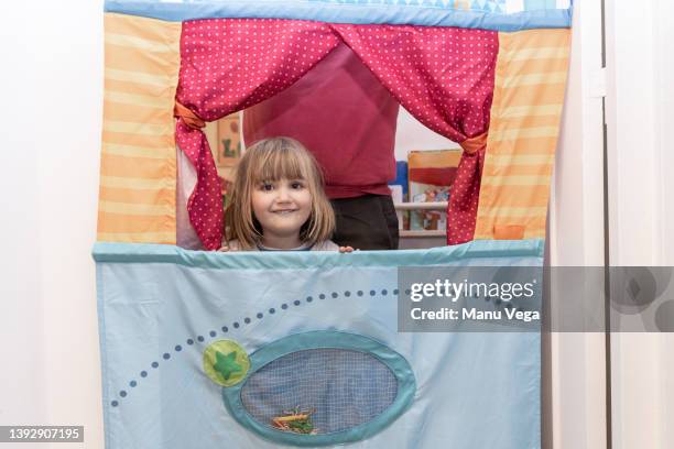 little girl leaning out of the window of a puppet theater at home, in the background her grandfather helping to set it up. - puppet show imagens e fotografias de stock