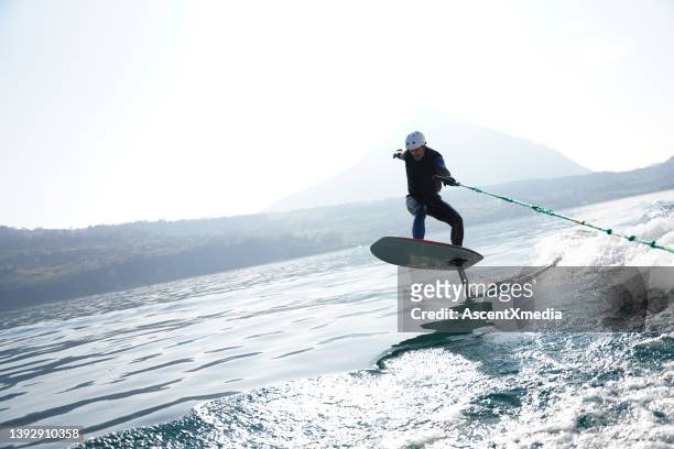 view of man riding wake foil behind motor boat - wakeboarding stock pictures, royalty-free photos & images