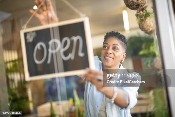 lgbtq+ woman hanging open sign in store window - open sign stock pictures, royalty-free photos & images