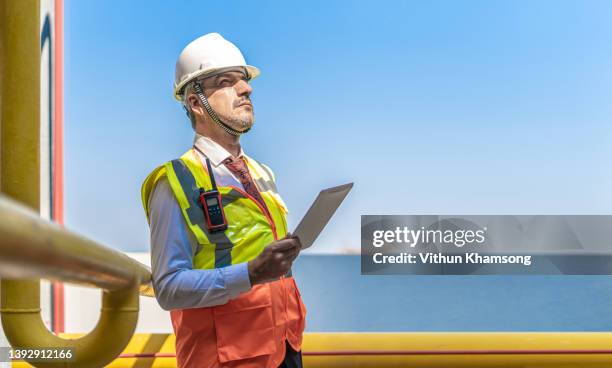 professional heavy industry engineer /worker wearing safety vest and hardhat. in the background pipeline industrial factory. - oil production platform stock pictures, royalty-free photos & images