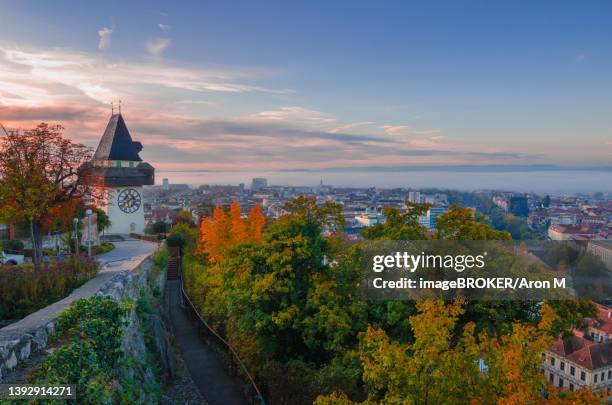 cityscape of graz and the famous clock tower (grazer uhrturm) on schlossberg hill, graz, styria region, austria, in autumn, at sunrise - turmuhr stock-fotos und bilder