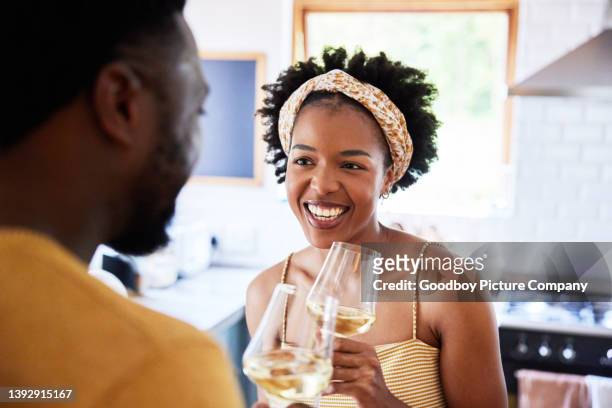 smiling woman talking with her husband over glasses of wine in their kitchen - boyfriend stock pictures, royalty-free photos & images
