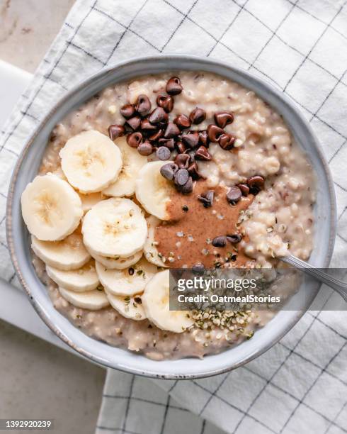overhead view of a bowl of creamy oatmeal with banana, almond butter, chocolate chips and hemp seeds - hemp seed fotografías e imágenes de stock