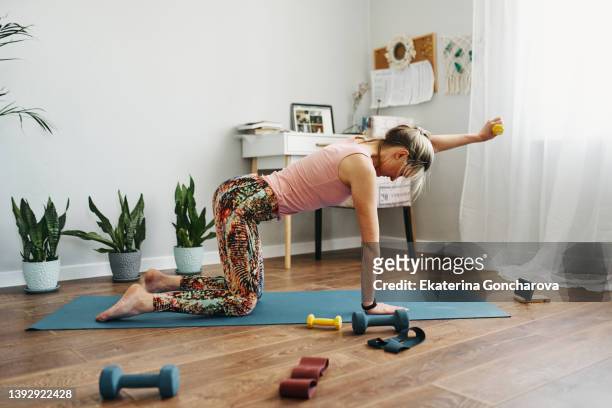 a woman is engaged in home fitness. woman working out with weights while exercising in home - pilates home stock pictures, royalty-free photos & images