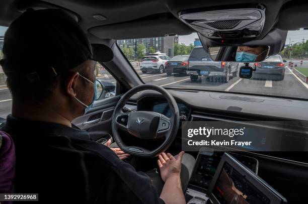 Safety driver" holds his hands away from the steering wheel as he sits in an Apollo Moon robotaxi on the road in a demonstration area as part of...