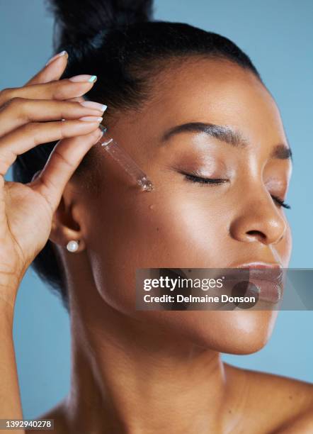 foto de estudio de una mujer joven aplicándose un aceite en la cara sobre un fondo azul - cuentagotas fotografías e imágenes de stock