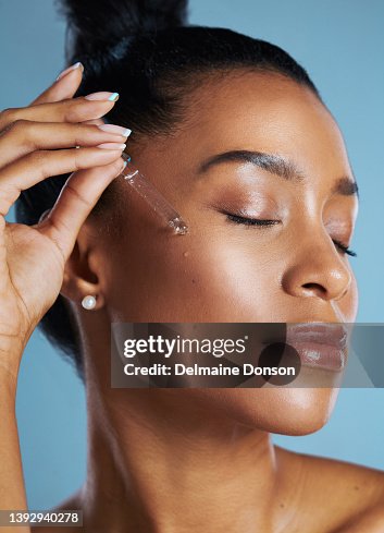 Studio shot of a young woman applying an oil to her face against a blue background Studio shot of a young woman applying an oil to her face against a blue background