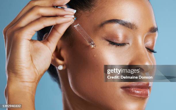 studio shot of a young woman applying an oil to her face against a blue background - face oil stock pictures, royalty-free photos & images