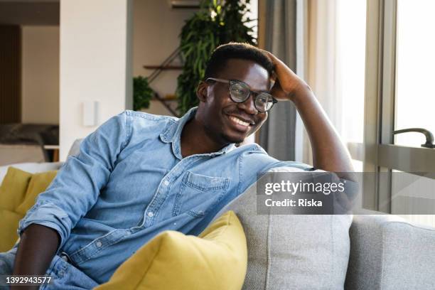 portrait of a young man relaxing on the couch - denim shirt stock pictures, royalty-free photos & images