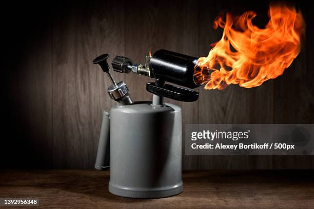close-up of fire in container on table against wall - blow torch stock pictures, royalty-free photos & images