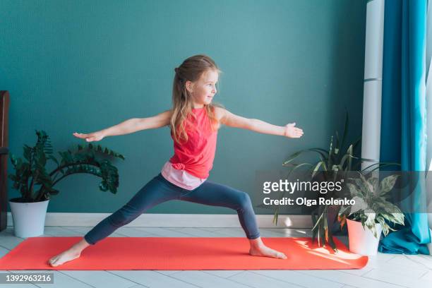 concentrated cute little barefoot girl doing sport yoga exercises, keeping hands up and making legs apart - children yoga stock-fotos und bilder