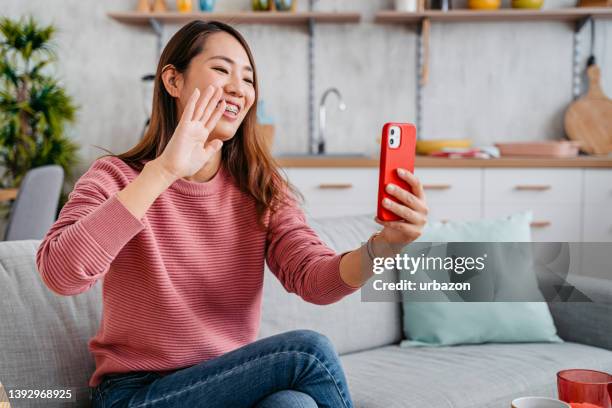 young woman having a video call with a friend using phone - friends laughing at iphone video stock pictures, royalty-free photos & images