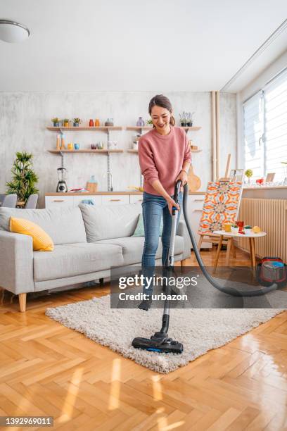 mujer joven aspirando su apartamento - home cleaning fotografías e imágenes de stock