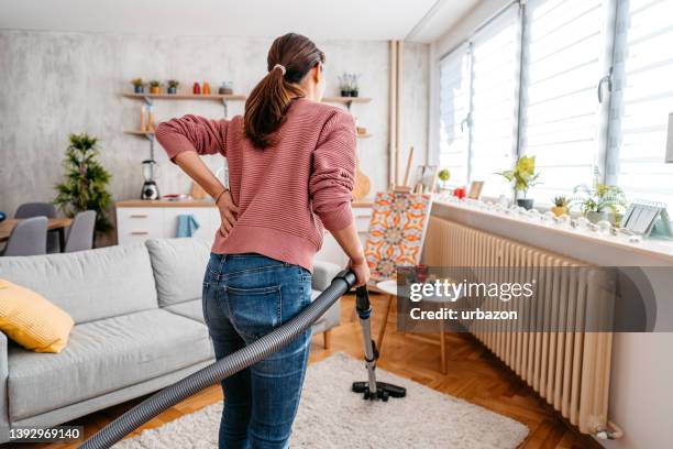 young woman vacuuming her apartment - backache stock pictures, royalty-free photos & images