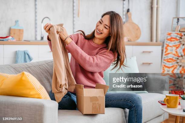 young woman unboxing a package with a new sweater - newly opened stock pictures, royalty-free photos & images