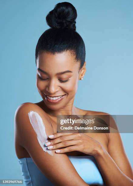 studio shot of a young woman applying lotion against a blue background - applying sunscreen stock pictures, royalty-free photos & images