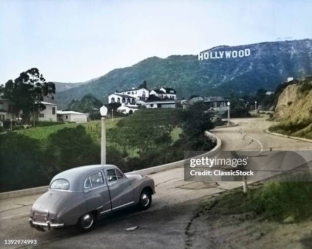 1950s Austin Car Driving Up a Road In The Hollywood Hills With the Hollywood Sign In the Distance Los Angeles California US.