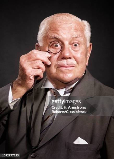 1950s 1960s Surprised Senior Businessman Man Looking At Camera Through Monocle With Funny Alarmed Facial Expression.