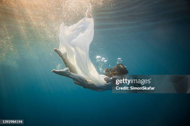 women with brown hair and white dress diving underwater in the sea, view from the side - mermaid stock pictures, royalty-free photos & images