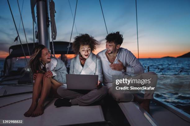 friends laughing and smiling while sitting on boat deck of a sailboat with a laptop during sunset - socorro island imagens e fotografias de stock