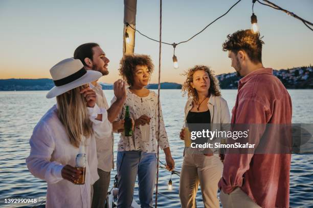 eine gruppe von freunden genießt einen warmen abend und trinkt einen drink auf dem bootsdeck eines segelboots auf dem meer, der insel und dem sonnenuntergang im hintergrund - on deck circle stock-fotos und bilder