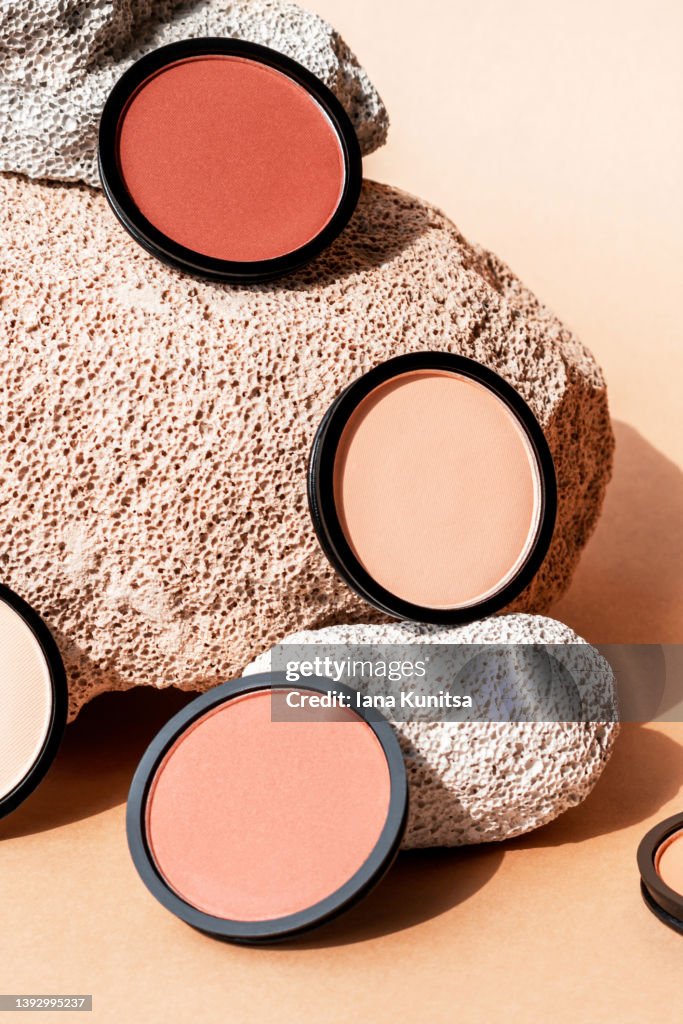 Compact face powder, blush and eyeshadow on beige background with porous stones. Vertical. Cosmetics for contouring.