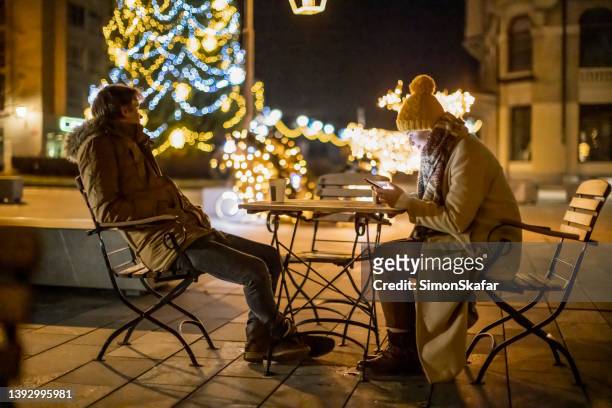 displeased boyfriend sitting with socially addicted girlfriend in cafe at night - bored girlfriend stock pictures, royalty-free photos & images