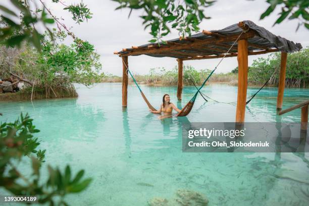 frau, die in der hängematte im wasser in der bacalar-lagune in mexiko ruht - luxury location stock-fotos und bilder