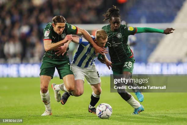 Lewis O'Brien of Huddersfield Town is challenged by Callum Brittain and Domingos Quina of Barnsley during the Sky Bet Championship match between...