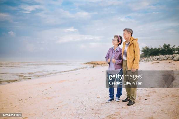 un couple de personnes âgées asiatiques chinoises à la plage regarde au loin avec des vêtements chauds - couple paysage asie photos et images de collection