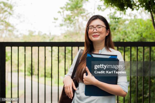 waist-up portrait of a young southeast asian female teacher outdoors inside the campus with copy space - teacher with folder stock pictures, royalty-free photos & images